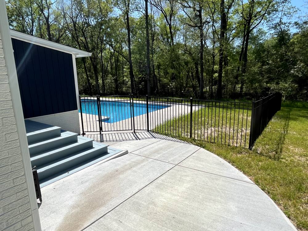 Black aluminum pool fence with a self closing gate beside a patio in the Midlands of South Carolina