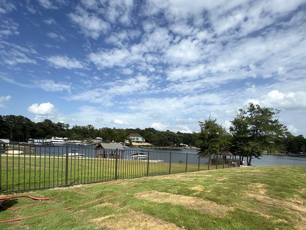 Black aluminum fence along a sloping lawn above a lake with boats at the dock in the Midlands of South Carolina