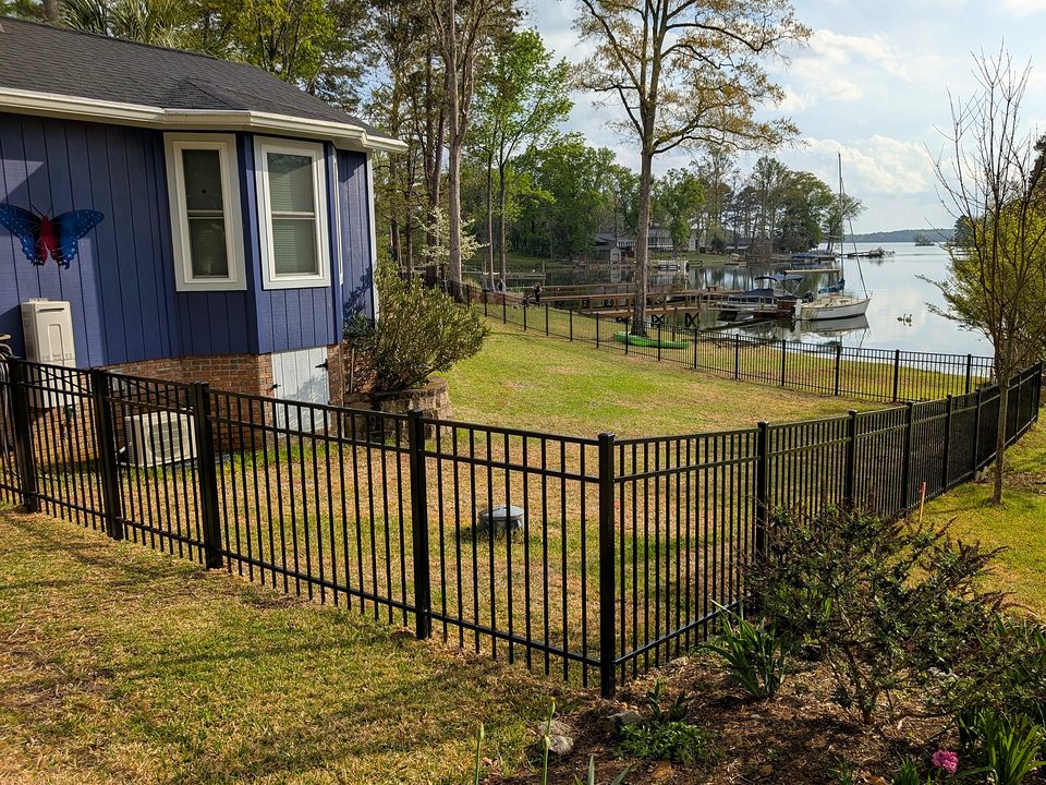 Black aluminum fence around a lakefront yard in Chapin, SC with a dock and a sailboat behind it