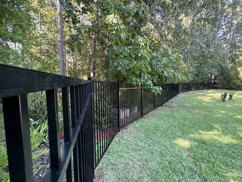 Long run of black aluminum fence along a green lawn beside the woods in the Midlands of South Carolina