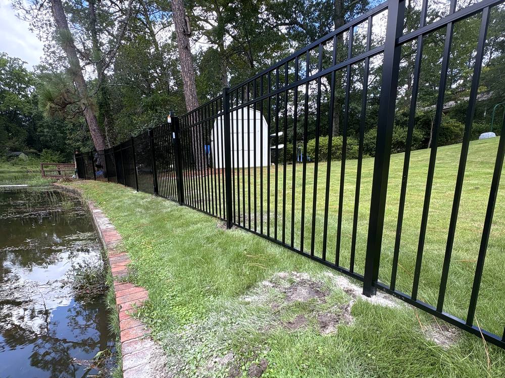 Black aluminum fence along a pond and a brick walk behind a home in the Midlands of SC