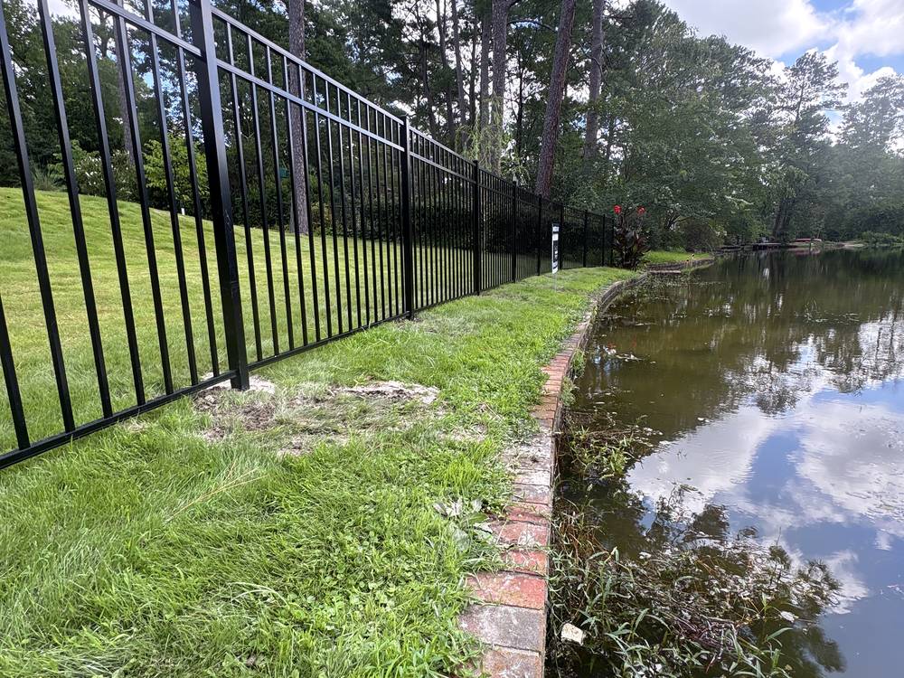 Black aluminum fence beside a brick bordered pond edge in the Midlands of South Carolina