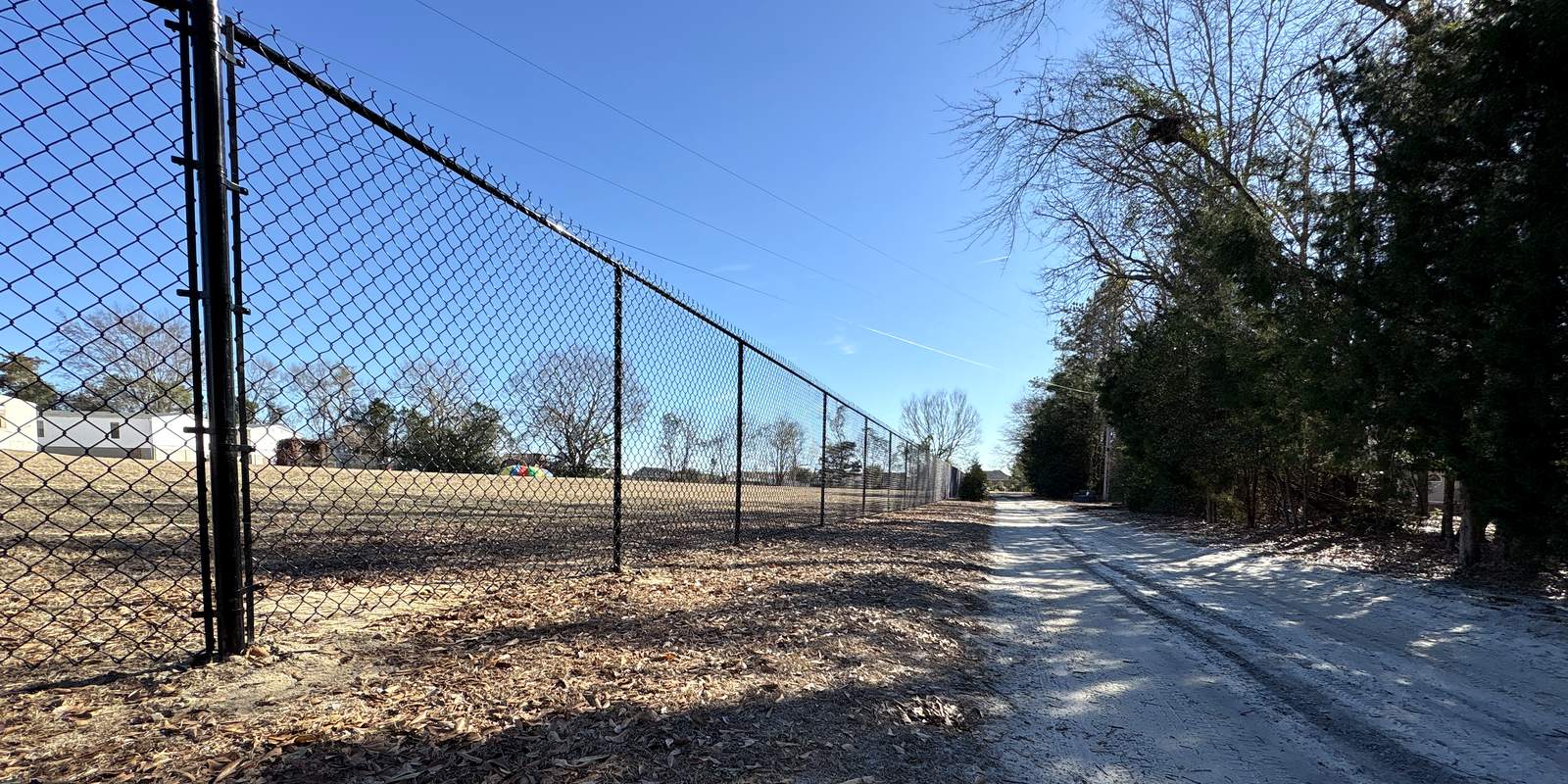 Black chain link fence running along a gravel path under a blue sky in the Midlands of South Carolina