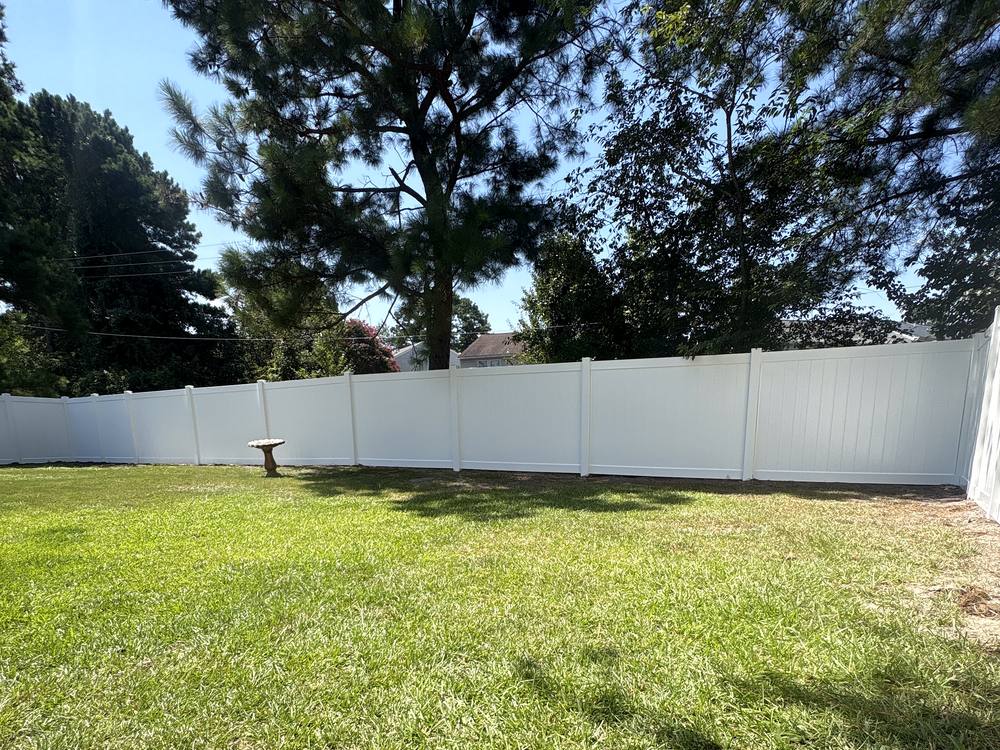 White vinyl privacy fence around a green backyard with a bird bath in the Midlands of South Carolina