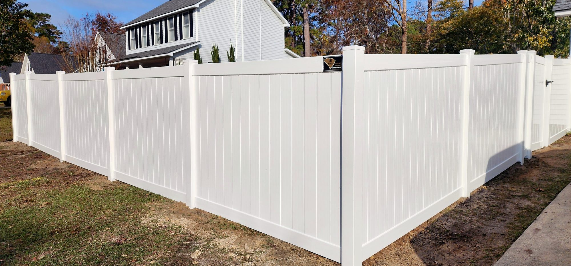 Corner of a new white vinyl privacy fence beside a two story home in the Midlands of South Carolina
