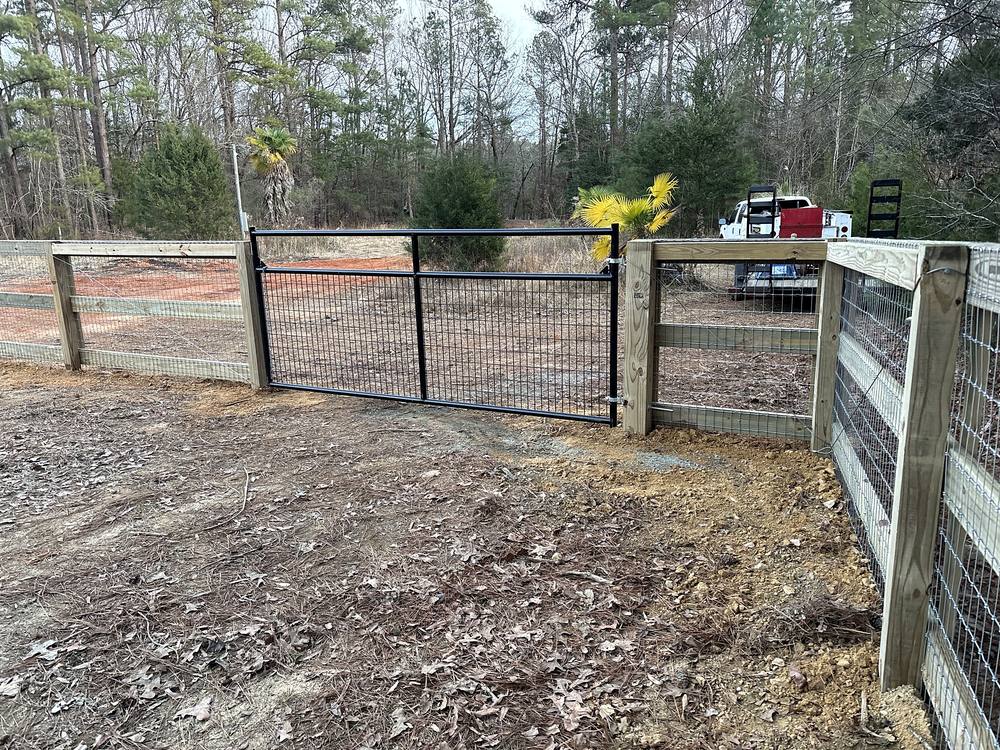 Wood and wire farm fence with a black steel gate beside a graded drive in the Midlands of South Carolina