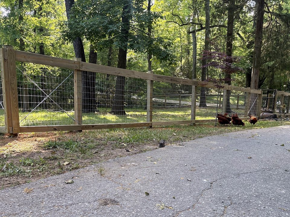 Wood and wire farm fence running along a drive in Chapin, SC with chickens beside it