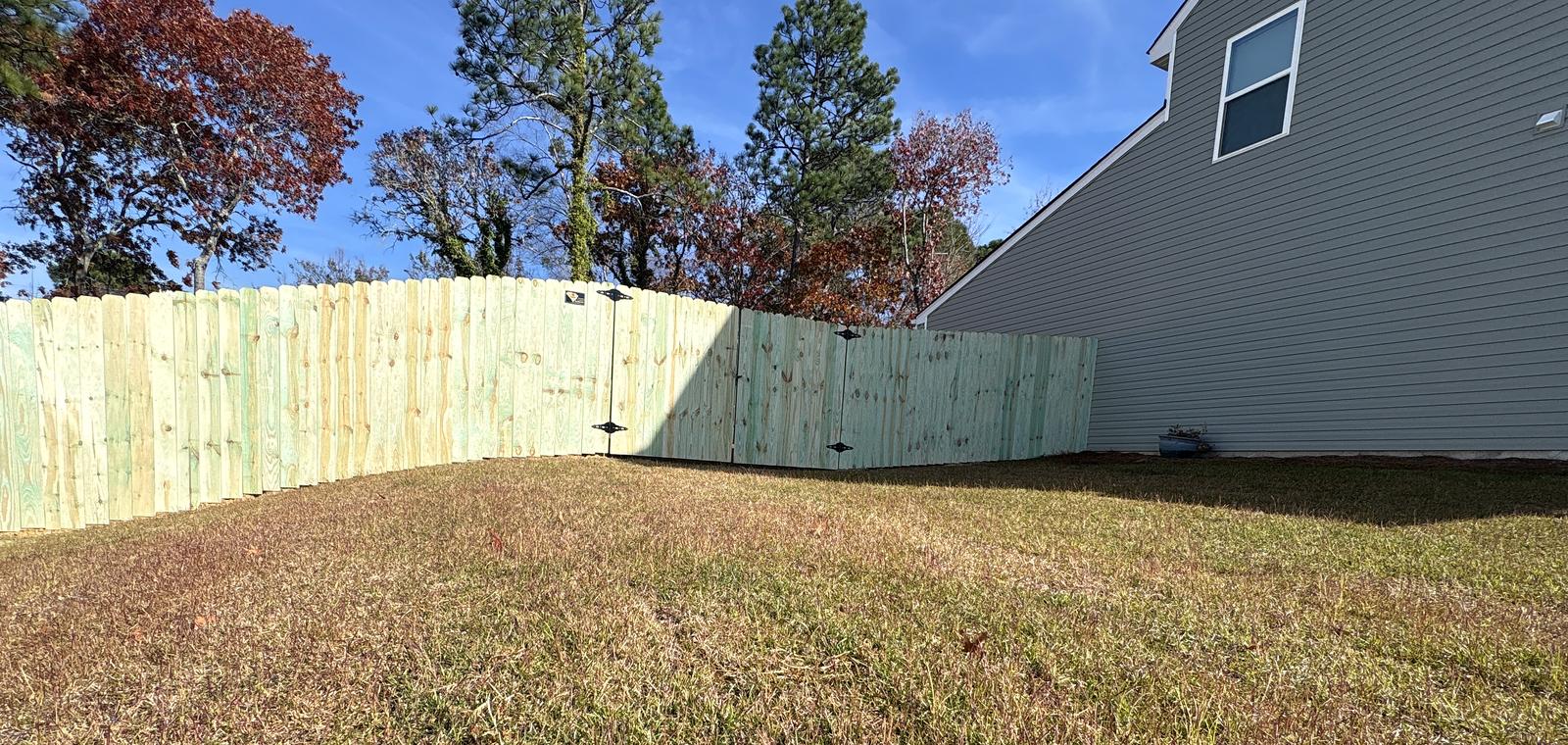 New wood privacy fence with a gate beside a home with fall trees in the Midlands of South Carolina