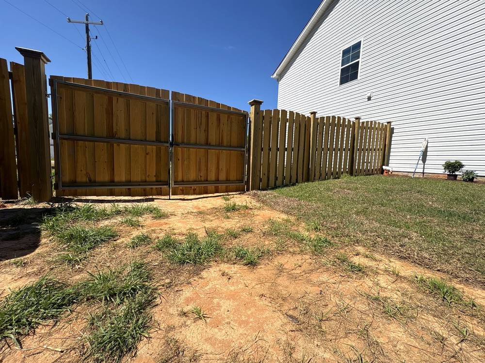 Wood shadowbox fence with an arched top double gate framed in steel beside a new home in Irmo, SC