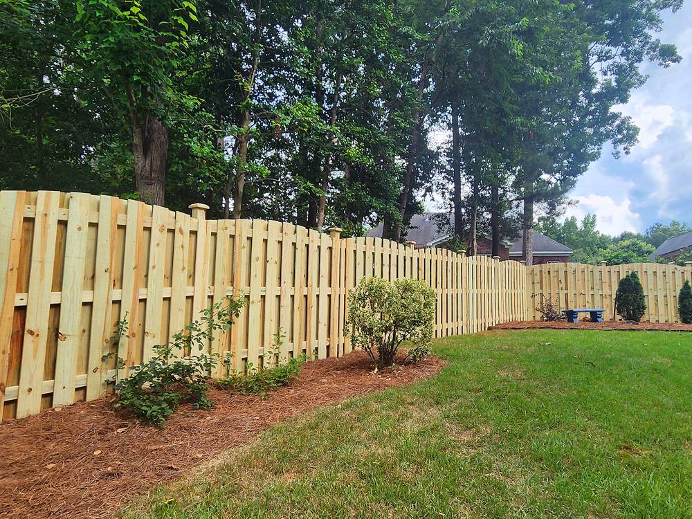 Wood shadowbox fence curving through a landscaped yard with new shrubs in the Midlands of South Carolina